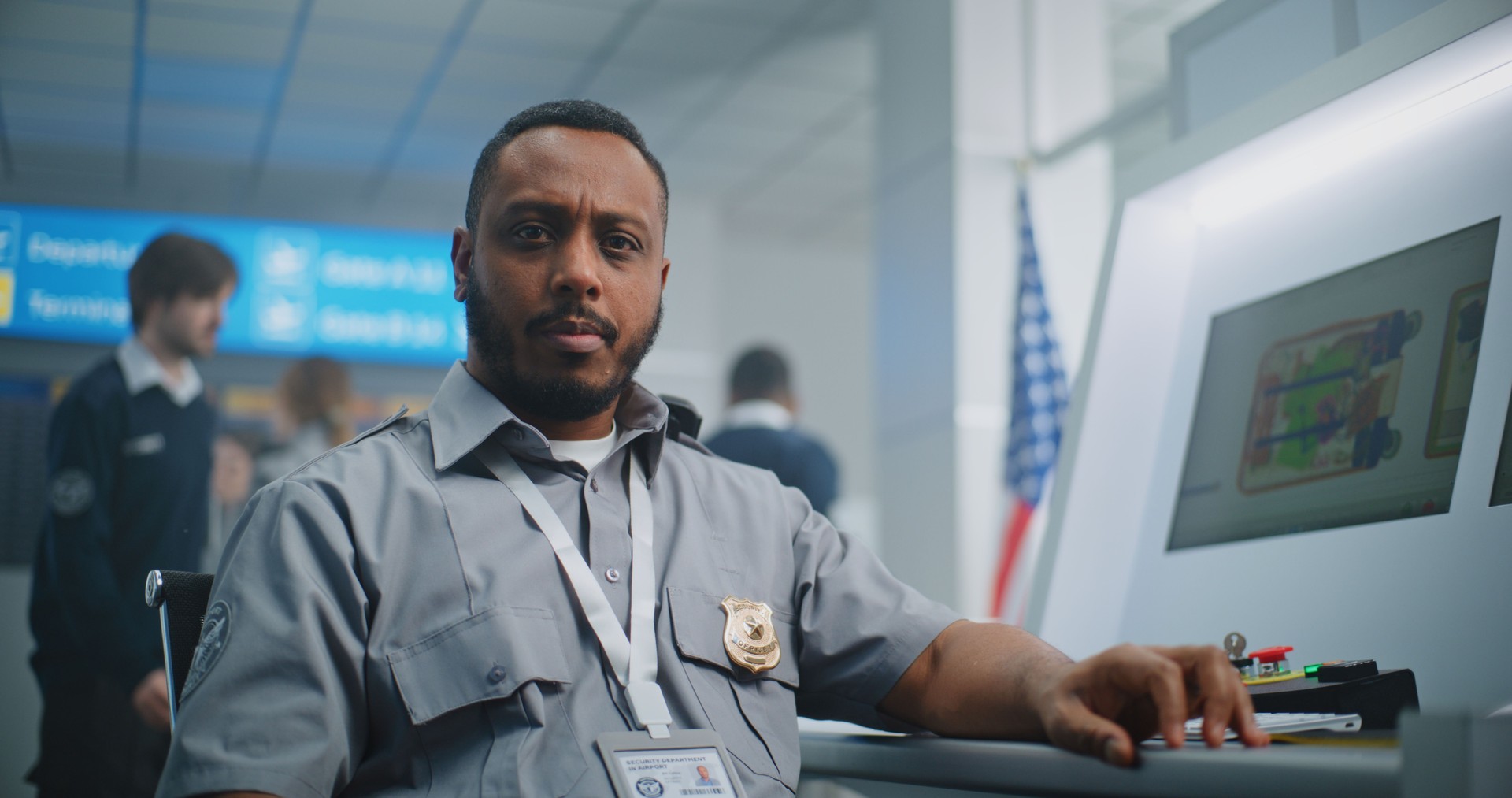 Portrait of TSA Worker Looking at Camera. Computer Screens Showing X-ray Images